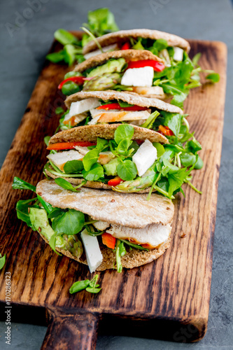Pita sandwiches stuffed with chicken, vegetables and cheese on wooden cutting board