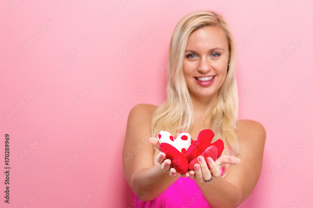 Happy young woman holding heart cushions on a pink background Happy young woman holding heart cushions on a pink background