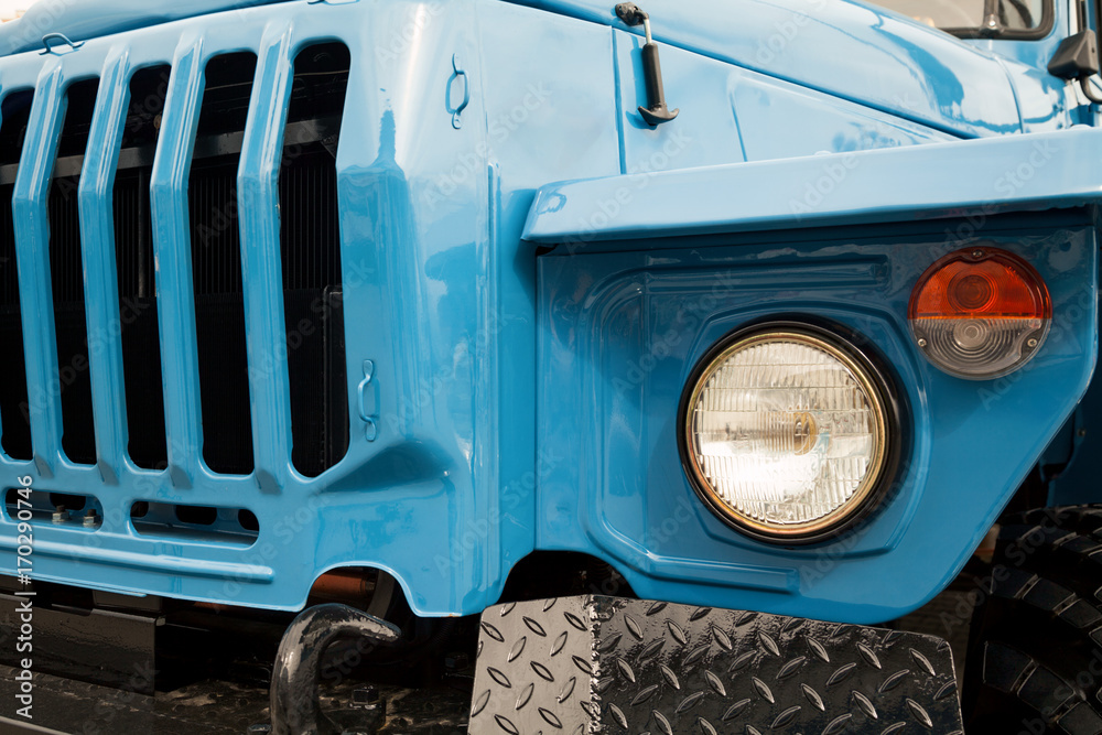 Blue truck front close-up with radiator grille and headlights. Heavy machinery background