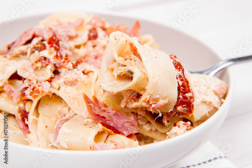 Pappardelle with cream, sun-dried tomatoes and smoked fish on a wooden background photo