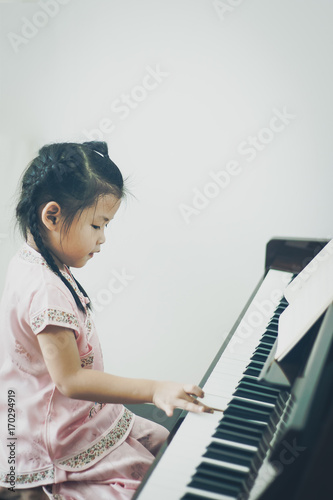 Cute little asian girl in traditional chinese dress playing piano with one hand. Digital color filter.