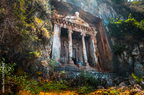 Amyntas rock tombs - 4th BC tombs carved in steep cliff. Tourist stands in front of the door. City of Fethiye, Turkey. photo