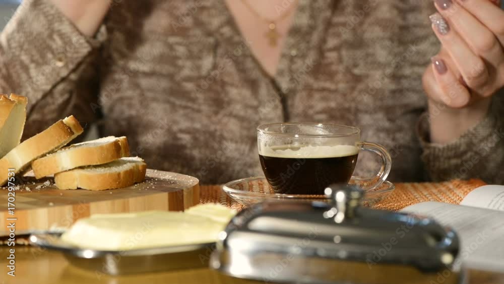 The woman with fine manicure has black coffee and eats sandwich from white loaf with butter The woman with fine manicure has black coffee and eats sandwich from white loaf with butter