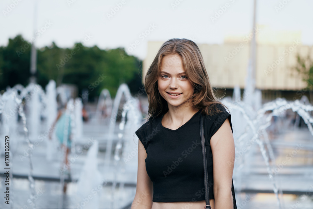 young woman standing by the fountain in the city, portrait