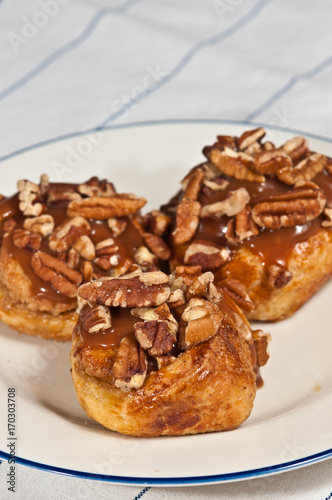 Pecan, cinnamon, croissant, sticky roles  on a round, white plate with a blue rim on a white table cloth with blue stripes