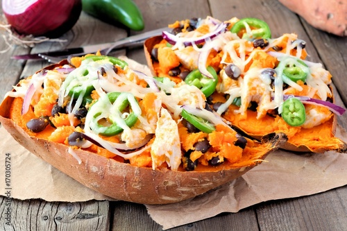 Baked sweet potatoes stuffed with chicken, vegetables and cheese, close up on a rustic wood background photo