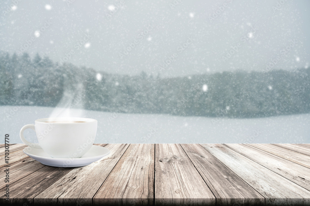 Cup of coffee on wooden table with winter snowfall covered forest. Vintage color tone and rustic style.