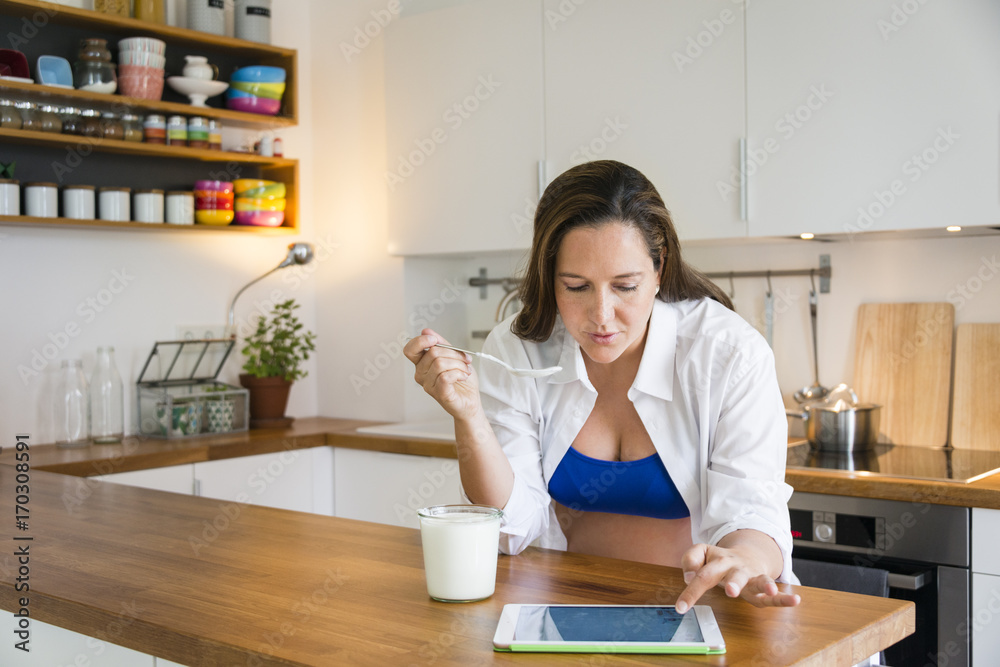 Pregnant woman eats yogurt while using tablet Pregnant woman eats yogurt while using tablet