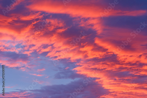 Part of sky with red clouds with sun positioned below and little piece of blue sky