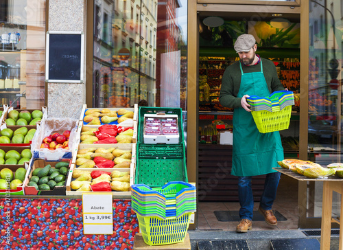 Grocer arranging shopper baskets in front of greengrocer's shop
