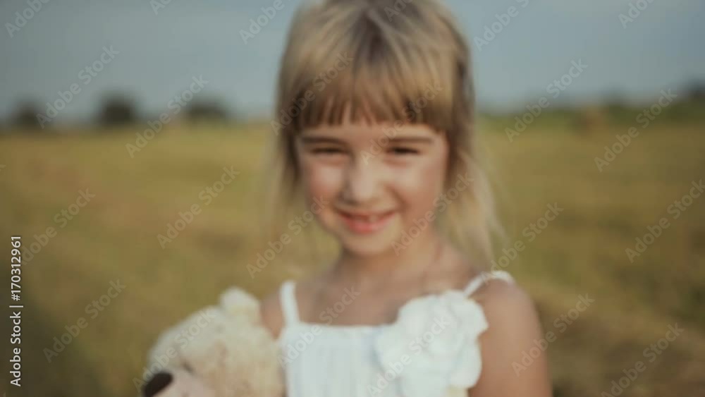 Little girl with beautiful dark eyes walks the field after the rain and is played by a toy bear Little girl with beautiful dark eyes walks the field after the rain and is played by a toy bear