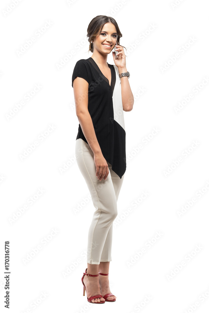 Young happy relaxed business woman talking on the mobile phone smiling and looking at camera. Full body length portrait isolated on white background Young happy relaxed business woman talking on the mobile phone smiling and looking at camera. Full body length portrait isolated on white background
