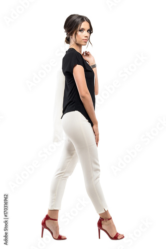 Side view of confident gorgeous business woman in suit walking and looking at camera. Full body length portrait isolated on white studio background