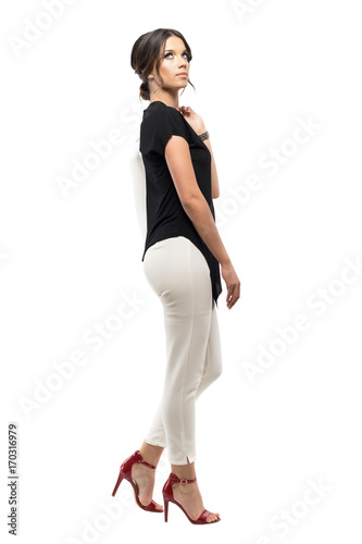 Side view of successful young business woman walking and carrying suit jacket looking up. Full body length portrait isolated on white background