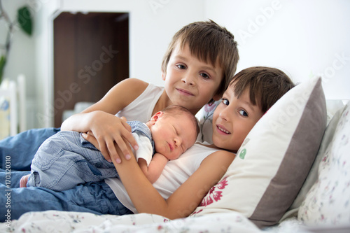Photos Two children, toddler and his big brother, hugging and kissing their newborn bab