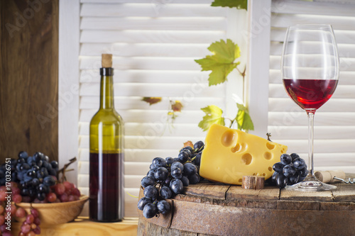 Still life of red wine with wooden keg. Wine bottle  glass of red wine with cheese and grape on a old wooden barrel.  Wine tasting and production concept.
