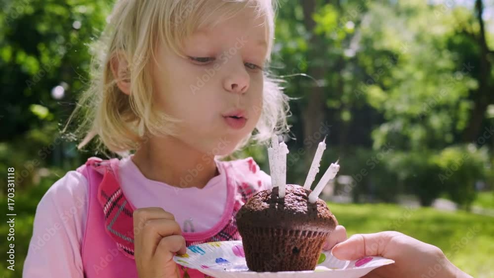 The little blond girl clapping her hands, dancing and blowing six candles out which burning on the chocolate cake. 4K