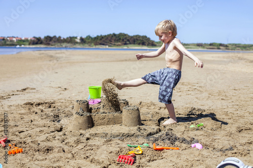 Boy kicking against sandcastle on beach