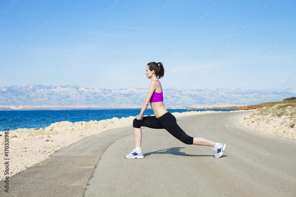 Young woman stretching leg on waterfront path Young woman stretching leg on waterfront path