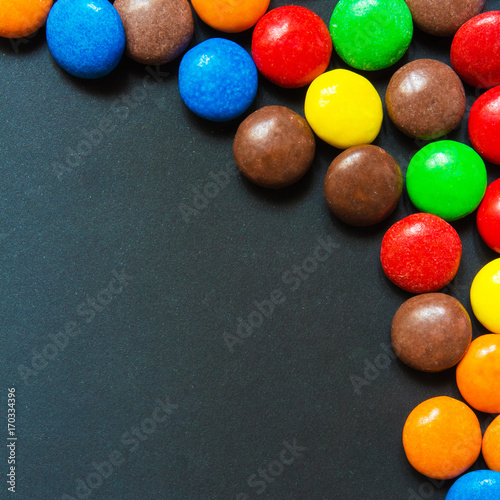 Multicolored sweets in the form of a dragee on a dark background pattern frame background
