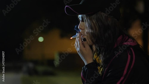 An angry sad teen girl with a cigarette. Night in park.