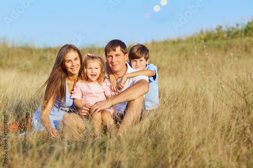 Happy family in nature. Mother, father, daughter and son are sitting on the grass in the park.