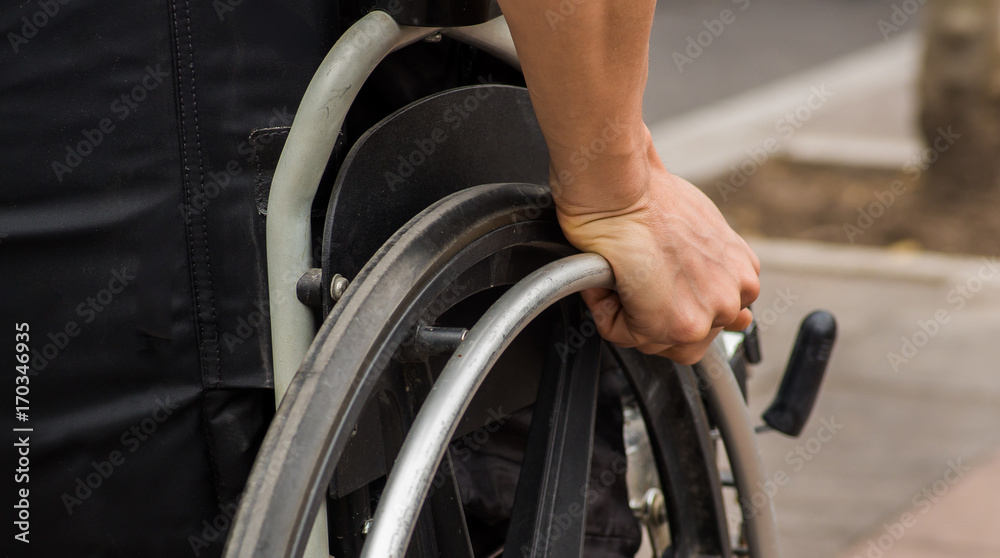 Close-up of male hand on wheel of wheelchair during walk in park Close-up of male hand on wheel of wheelchair during walk in park