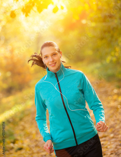 Young brunette woman running in autumn forest listening to mps music