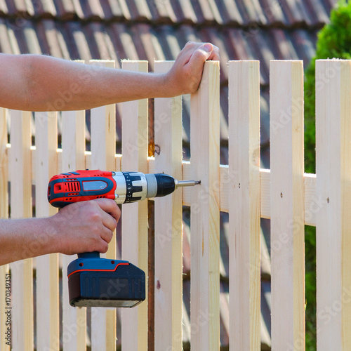 Man hands building wooden fence with a drill and screw. DIY concept. Close up of his hand and tool.