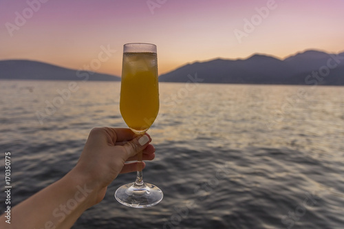 рука держит фужер с коктейлем на фоне моря и закат 