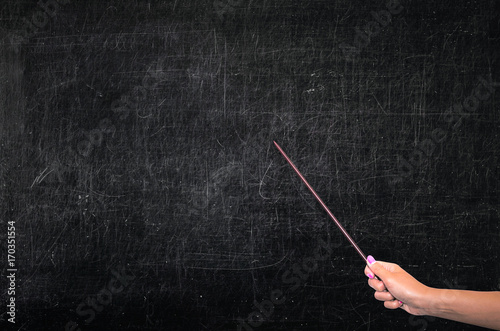 The teacher shows a pointer to an empty school chalkboard with copy space. Theme of the lesson, education concept.