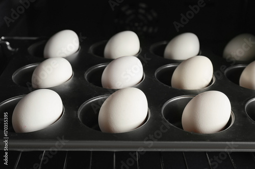 Muffin tin with hard boiled eggs in oven, closeup