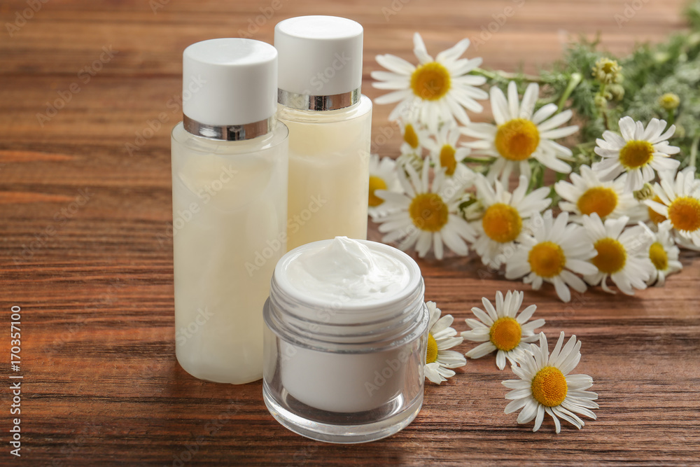 Two bottles and cosmetic jar with chamomiles on table Two bottles and cosmetic jar with chamomiles on table