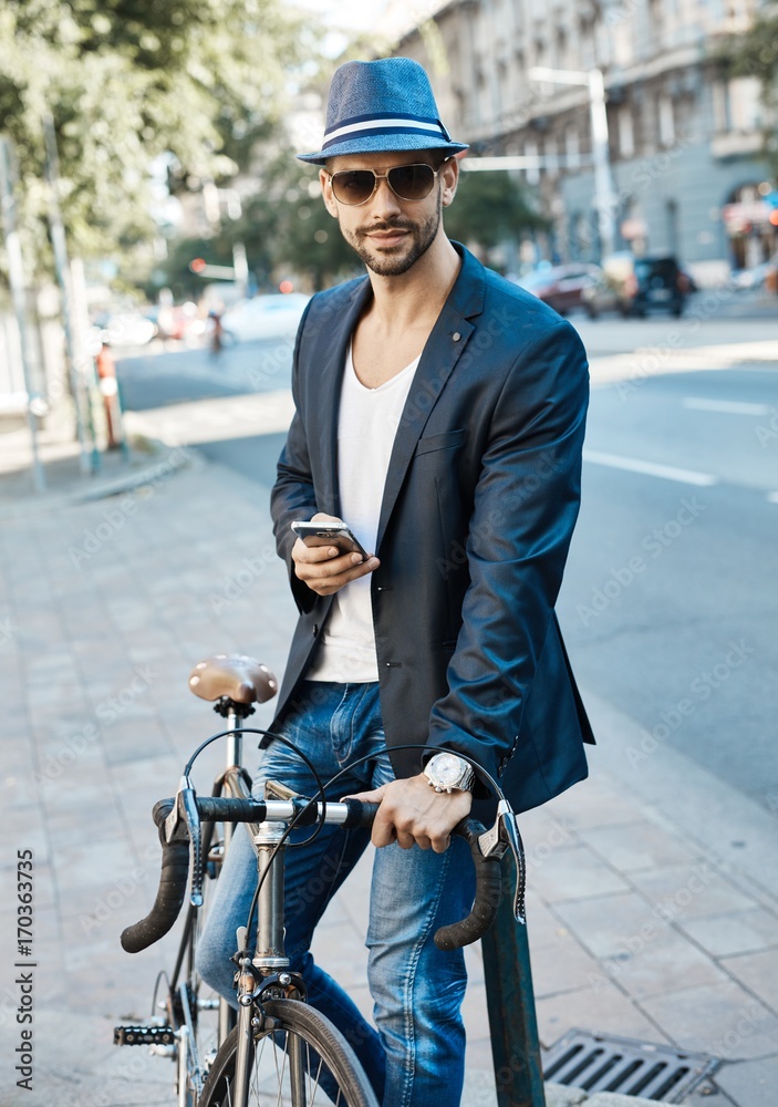 Obraz premium Stylish young man on street with bicycle and phone