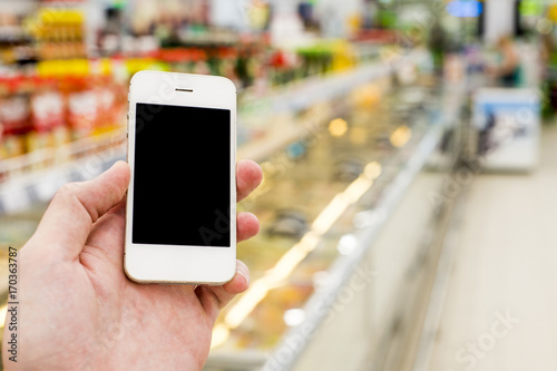 Man hand holding mobile smart phone on Supermarket blur background, business concept