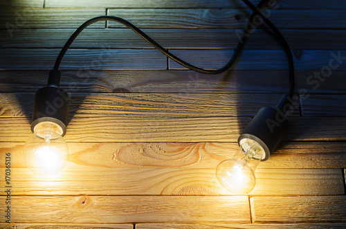 Two burning incandescent bulbs on a wooden background. A layout with an empty space for your text photo