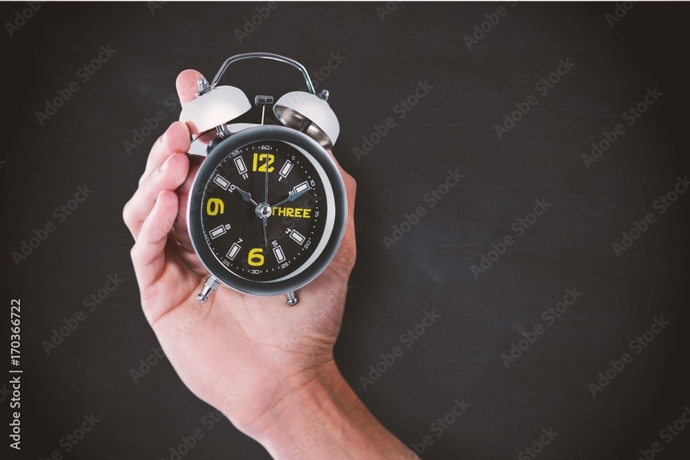 Composite image of cropped hand of man holding alarm clock