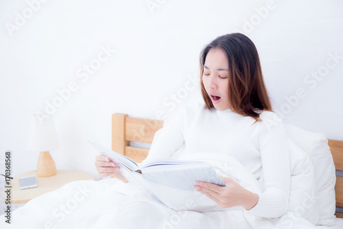 Asian woman reading a book and smiling in bedroom. lifestyle concept.