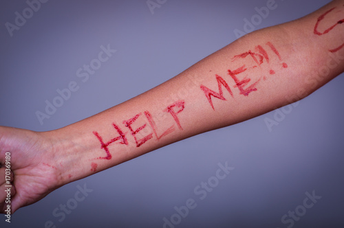 Close up of a young depressive woman, with her arm bleeding with the help word written in her arm with a knife, in a blurred background photo