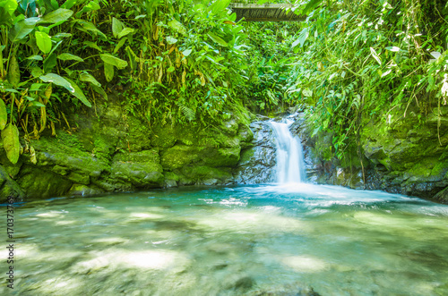 Beautiful small waterfall located inside of a green forest with stones in river at Mindo