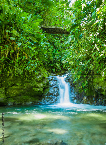 Beautiful small waterfall located inside of a green forest with stones in river at Mindo