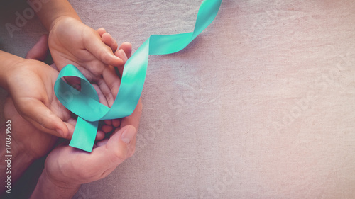 Adult and child hands holding Teal Ribbon, toning panoramic banner background, Ovarian Cancer, cervical Cancer, PCOS and sexual assault awareness photo