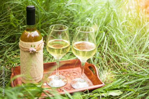 Fotografie White wine in the bottle and wine glasses on the wooden salver at the park