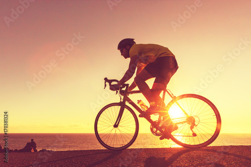 Road bike cyclist sports athlete biking outdoors silhouette near ocean. Professional triathlete riding bike on an open road to the sunset. Active healthy man sport lifestyle.