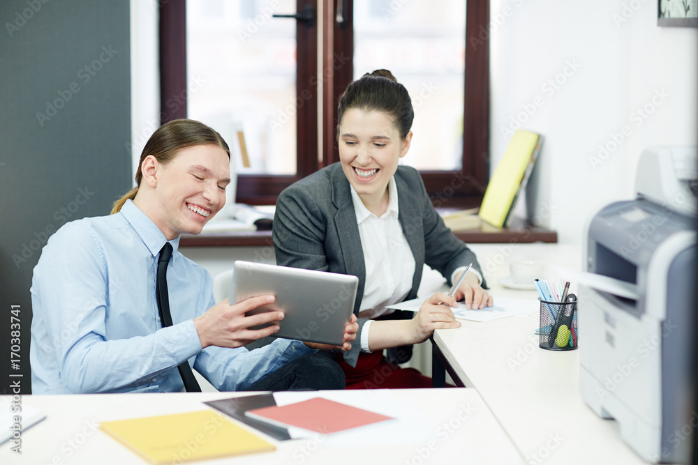 Cheerful managers reading online data or watching curious video in tablet