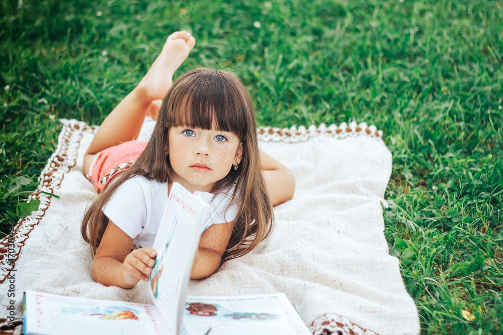 little beautiful girl lie on grass with book looking at camera little beautiful girl lie on grass with book looking at camera