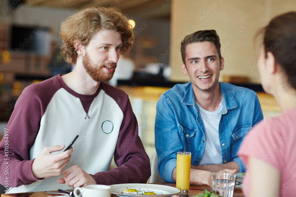 Happy guys talking to their groupmate by lunch between classes in college cafe Happy guys talking to their groupmate by lunch between classes in college cafe