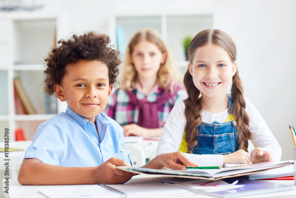 Friendly classmates reading book of tales at lesson Friendly classmates reading book of tales at lesson