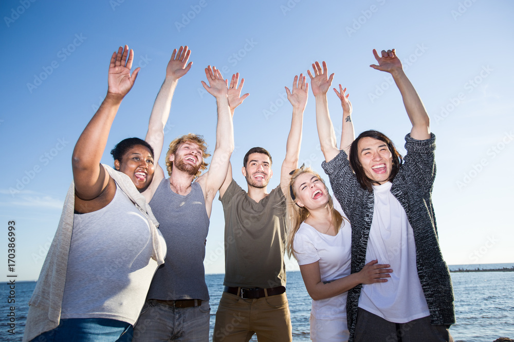 Laughing friends raising hands while enjoying beach party on summer day Laughing friends raising hands while enjoying beach party on summer day