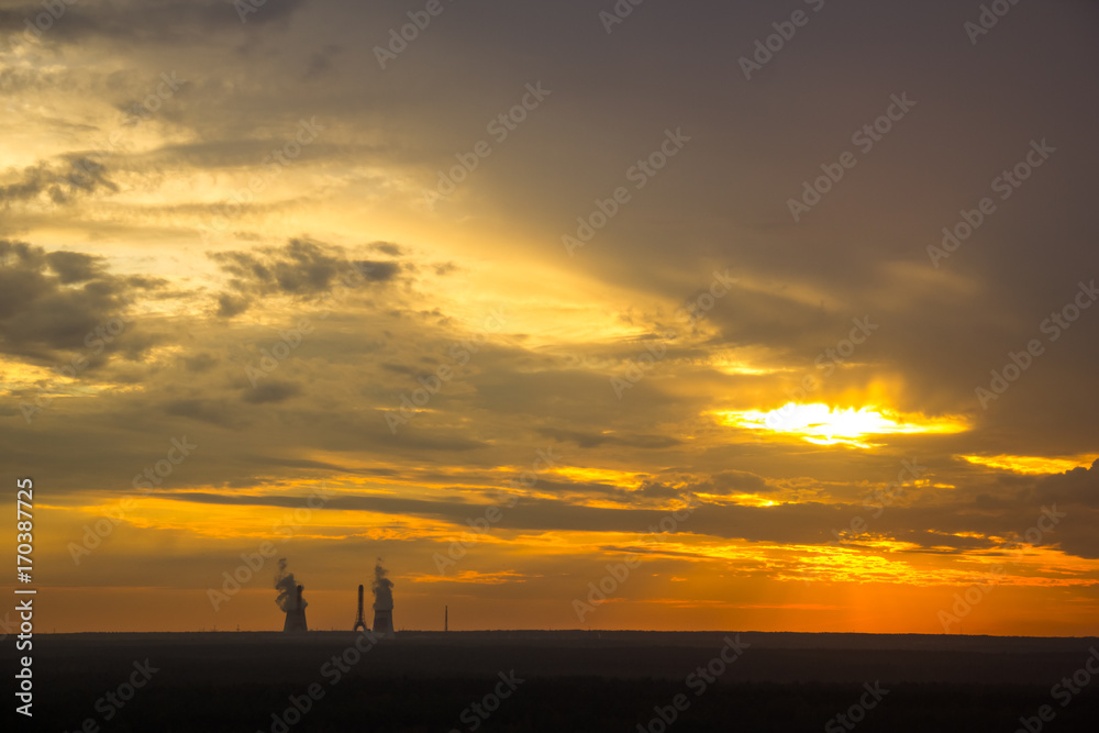 the smoke from the chimney at sunset. Colorful dramatic sunset in industrial zone of city. Silhouettes of houses and chimneys with smoke. Copy space
